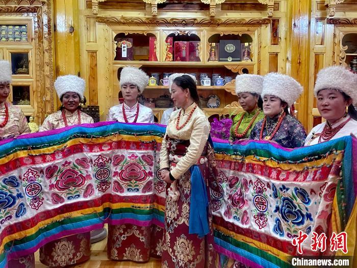 圖為女性展示村民自發(fā)繡制的“百米五彩哈達(dá)”?！±钣穹?攝